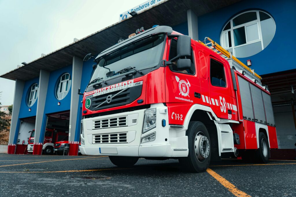 A modern fire truck parked outside a blue urban fire station, ready for emergency response.