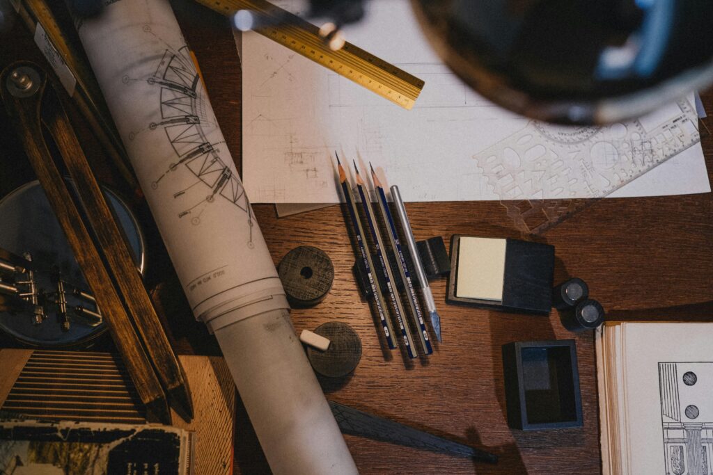 A cluttered workspace with architectural tools, blueprints, and pencils for design work.